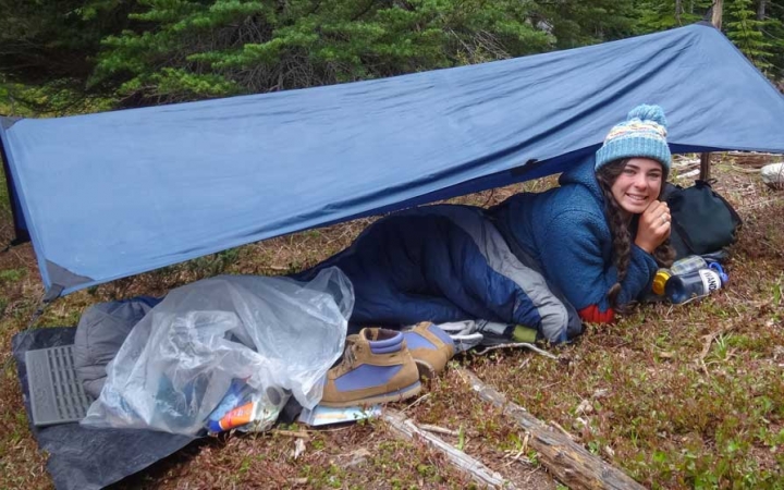 a person smiles while laying under a tarp in the woods on an outward bound expedition 
